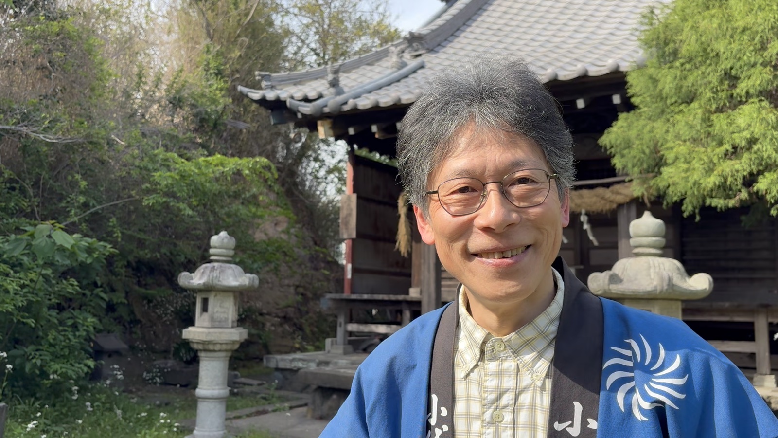 地域の祠の前に立つ和田さん。お囃子会の法被姿で微笑む