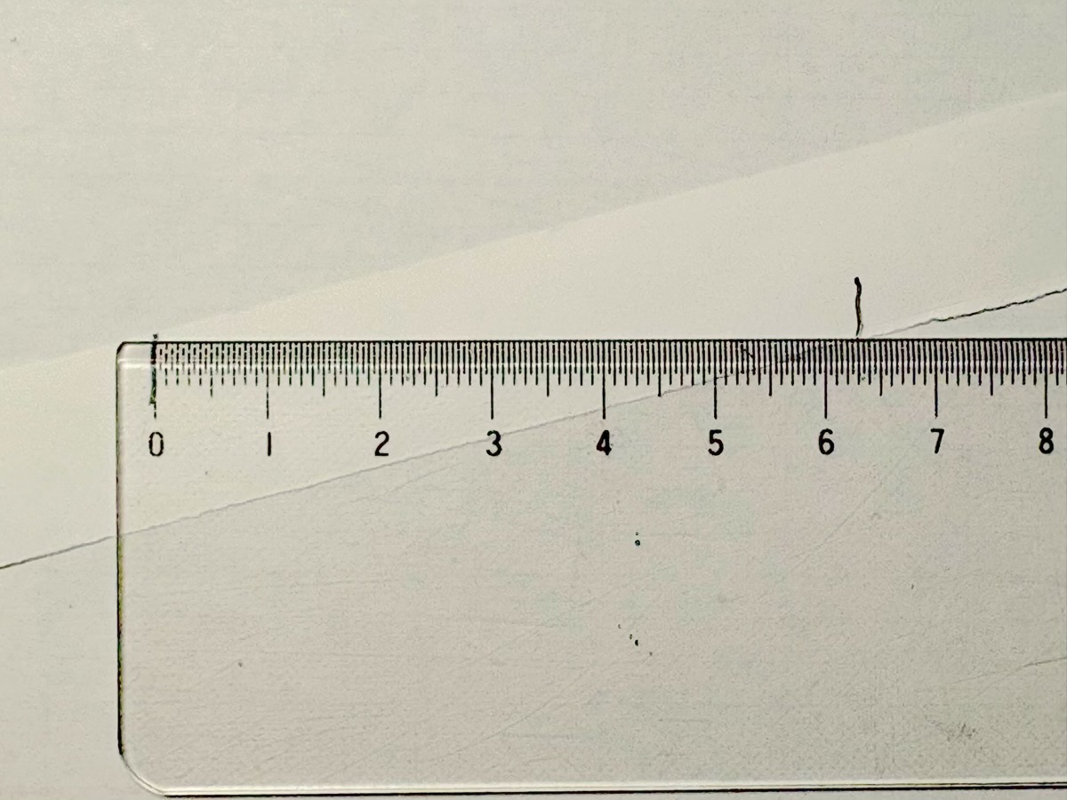 ほどいた紙を物差しに当てて、印と印の間の長さを読んでいる。約6.3cmの位置に印がある